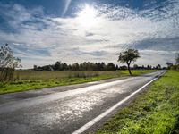 a lone highway through the countryside under a clear sky with clouds and trees, in front of a field