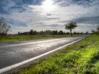 a lone highway through the countryside under a clear sky with clouds and trees, in front of a field