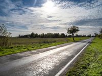 a lone highway through the countryside under a clear sky with clouds and trees, in front of a field