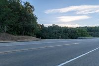 a highway with a sign and a man on his bike in the foreground, near trees