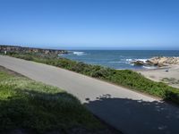 an empty paved road alongside a beach and the ocean on the horizon, with a clear blue sky