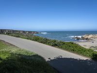 an empty paved road alongside a beach and the ocean on the horizon, with a clear blue sky