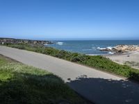 an empty paved road alongside a beach and the ocean on the horizon, with a clear blue sky