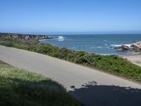 an empty paved road alongside a beach and the ocean on the horizon, with a clear blue sky