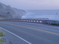 a couple of vehicles are driving on the side of a highway near the ocean and cliffs