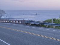 a couple of vehicles are driving on the side of a highway near the ocean and cliffs