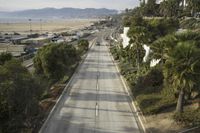 a empty road next to the ocean with palm trees on both sides and buildings near by