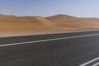 a car drives down a highway near the desert hills and dunes on a clear day