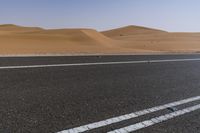 a car drives down a highway near the desert hills and dunes on a clear day