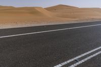 a car drives down a highway near the desert hills and dunes on a clear day