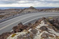 a road going up a mountain next to a large rock formation in the distance with a winding section on either side