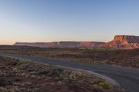 two men are riding down the highway in the middle of a big mountain range at sunset