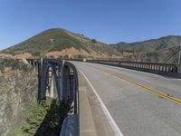 the road passes under this high bridge over water and hills, while the road passes a narrow one lane highway