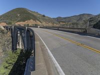 the road passes under this high bridge over water and hills, while the road passes a narrow one lane highway