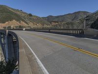 the road passes under this high bridge over water and hills, while the road passes a narrow one lane highway