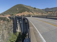 the road passes under this high bridge over water and hills, while the road passes a narrow one lane highway