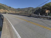 the road passes under this high bridge over water and hills, while the road passes a narrow one lane highway