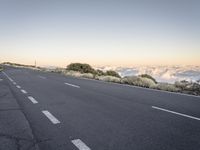 a highway on the top of a mountain overlooking a valley and clouds below it with a road sign posted in it