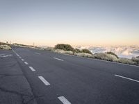 a highway on the top of a mountain overlooking a valley and clouds below it with a road sign posted in it