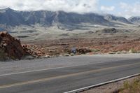 an asphalt street lined with rocky mountains near the ocean or desert with two people on it