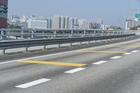 a view from an overpass of highway with two white arrows on the roadway and a few buildings in the background