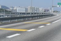 a view from an overpass of highway with two white arrows on the roadway and a few buildings in the background