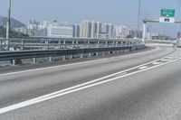 a view from an overpass of highway with two white arrows on the roadway and a few buildings in the background