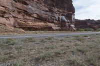 a person riding a motorcycle along a narrow road through rocks and sand cliffs a grassy area on both sides