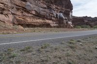 a person riding a motorcycle along a narrow road through rocks and sand cliffs a grassy area on both sides