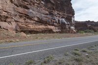 a person riding a motorcycle along a narrow road through rocks and sand cliffs a grassy area on both sides