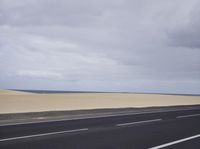 there is a highway with sand dunes in the background in this photo, the road goes to the right