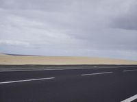 there is a highway with sand dunes in the background in this photo, the road goes to the right