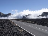 the view of a highway surrounded by lava and clouds, with a biker driving in the distance