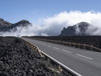 the view of a highway surrounded by lava and clouds, with a biker driving in the distance