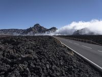 the view of a highway surrounded by lava and clouds, with a biker driving in the distance