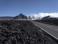 the view of a highway surrounded by lava and clouds, with a biker driving in the distance