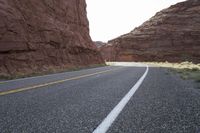 a person riding a motorcycle along a narrow road through rocks and sand cliffs a grassy area on both sides