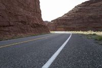 a person riding a motorcycle along a narrow road through rocks and sand cliffs a grassy area on both sides