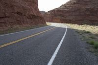 a person riding a motorcycle along a narrow road through rocks and sand cliffs a grassy area on both sides