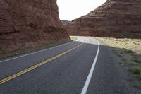 a person riding a motorcycle along a narrow road through rocks and sand cliffs a grassy area on both sides