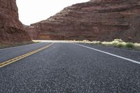 a person riding a motorcycle along a narrow road through rocks and sand cliffs a grassy area on both sides