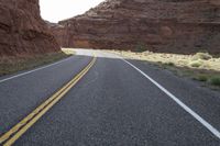 a person riding a motorcycle along a narrow road through rocks and sand cliffs a grassy area on both sides