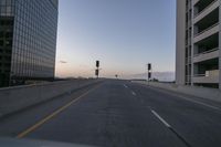 the car is traveling down a highway towards buildings in the city during a dusk or sunrise