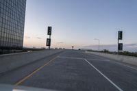 the car is traveling down a highway towards buildings in the city during a dusk or sunrise