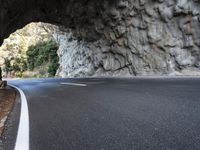 an arched tunnel on an empty highway near trees and shrubss in the mountains with road markings