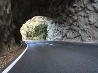 an arched tunnel on an empty highway near trees and shrubss in the mountains with road markings