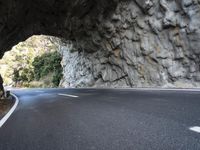 an arched tunnel on an empty highway near trees and shrubss in the mountains with road markings