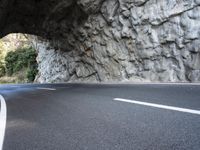 an arched tunnel on an empty highway near trees and shrubss in the mountains with road markings