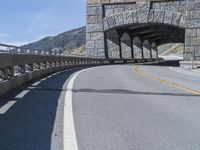 a tunnel leading to a highway near mountains in a scenic setting with the road's railings pointing out