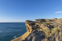 a person is hiking on a cliff above the water with a sky background, at a beach